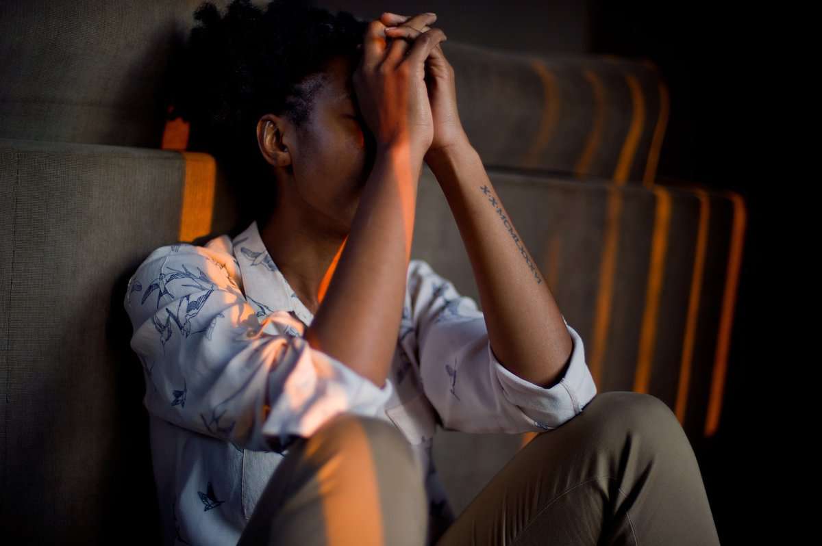 a woman with mental illness sitting on a couch holding her hands to her face.