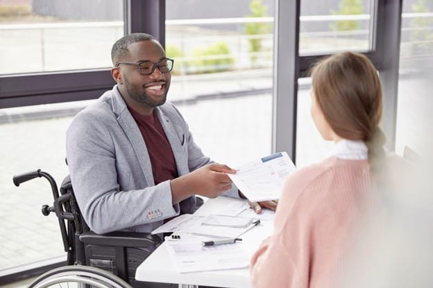 A man in a wheelchair talking to a woman in an office.